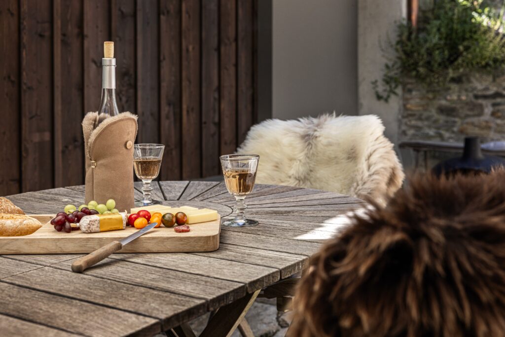 Lammfell-Weinkühler auf Terrassentisch mit Weingläsern und Käseplatte – Fell-shop.ch